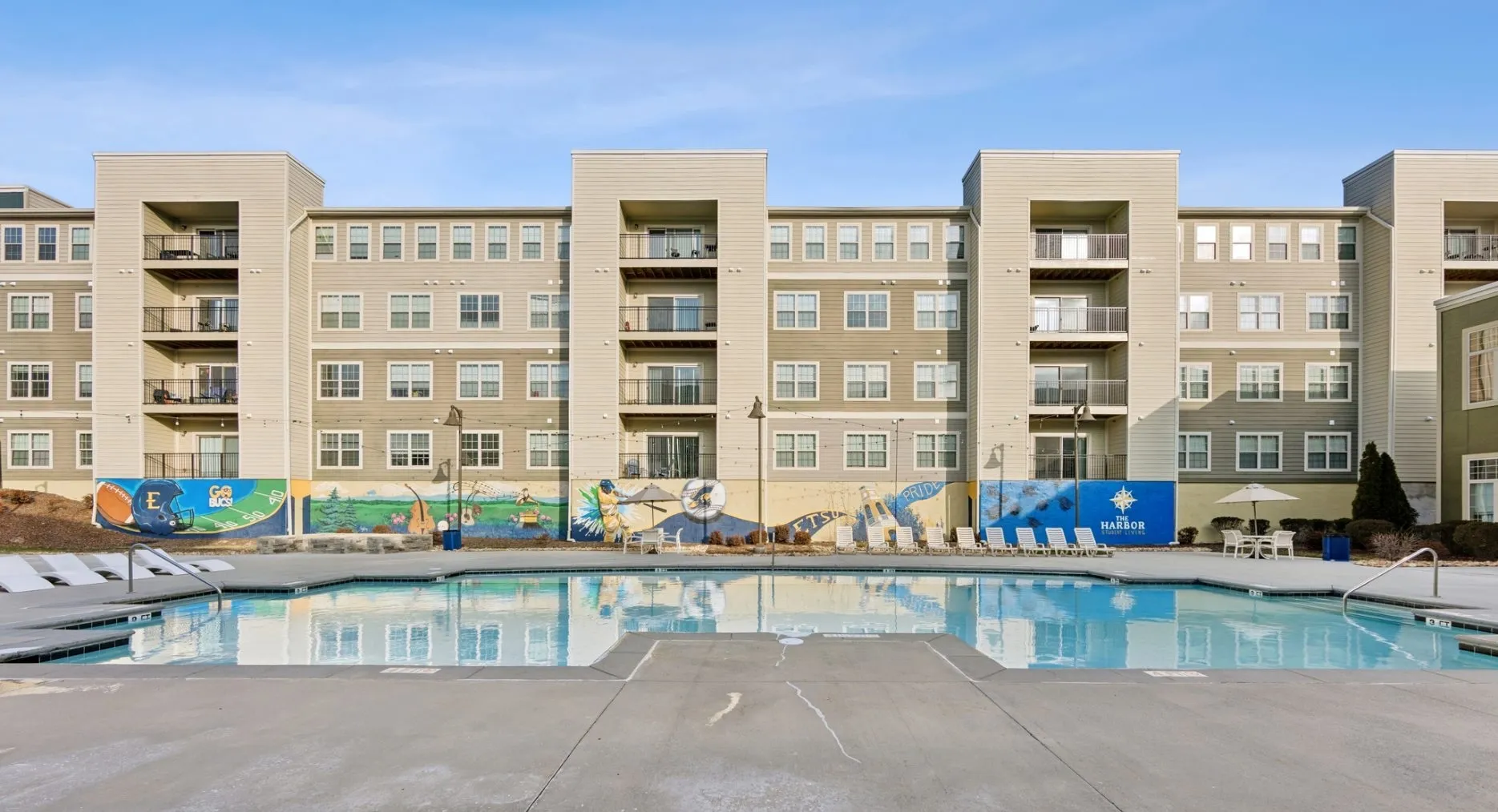 A large swimming pool in a courtyard with a paved patio, lounge seating, and potted plants.